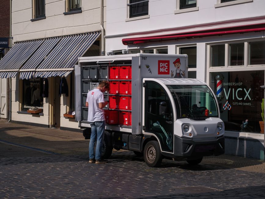 A courier organizing packages in an electric delivery van on a city street.